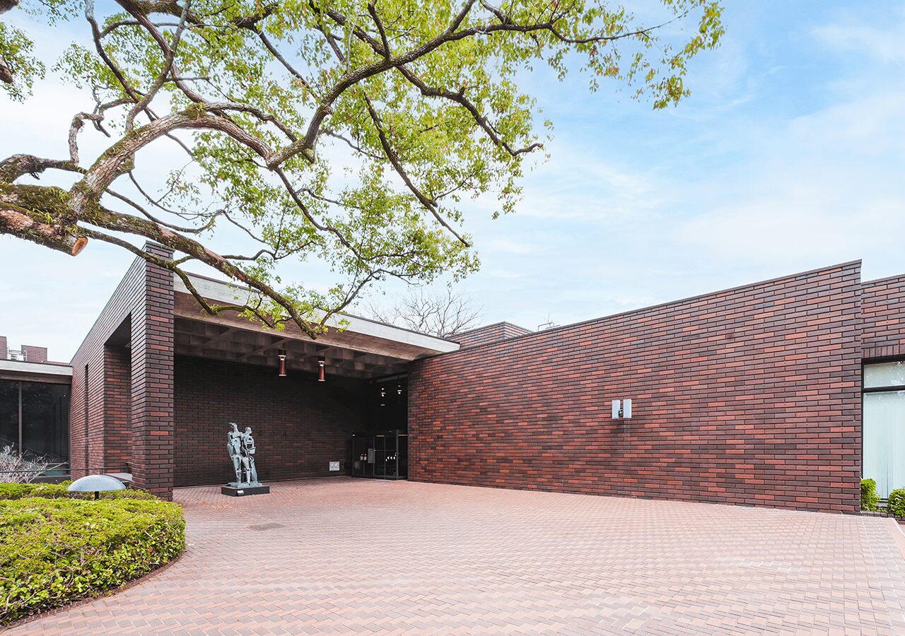 大木の下に建つレンガ張りの建築の外観